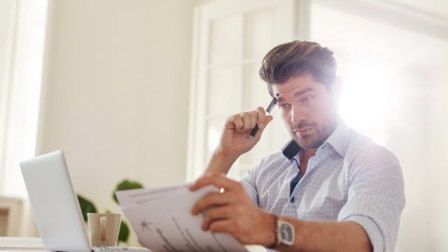 man with laptop looking at papers