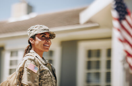 Servicewoman standing in front of her home with American flag in the background