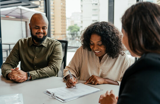 Husband and wife sitting at a table signing mortgage paperwork in attorney's office